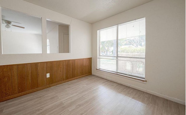 spare room with ceiling fan, light hardwood / wood-style floors, and wood walls