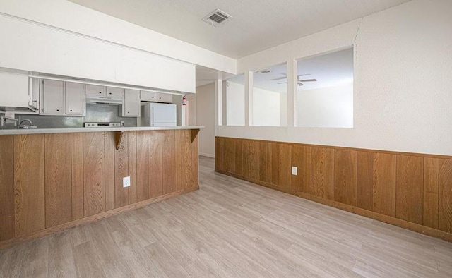 kitchen with a breakfast bar, wooden walls, white refrigerator, light hardwood / wood-style floors, and kitchen peninsula