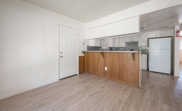 kitchen with a textured ceiling, a peninsula, freestanding refrigerator, and light wood-style floors