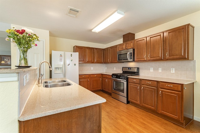 kitchen with sink, backsplash, stainless steel appliances, light stone countertops, and light wood-type flooring