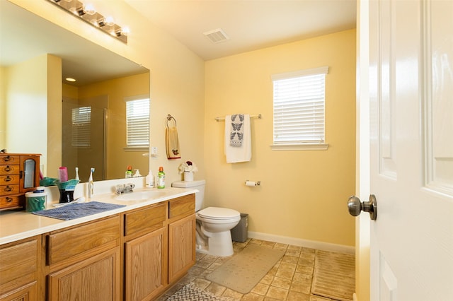 bathroom with vanity, a shower with door, toilet, and a healthy amount of sunlight