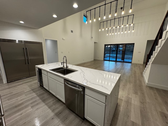 kitchen featuring sink, light stone counters, stainless steel appliances, a kitchen island with sink, and white cabinets