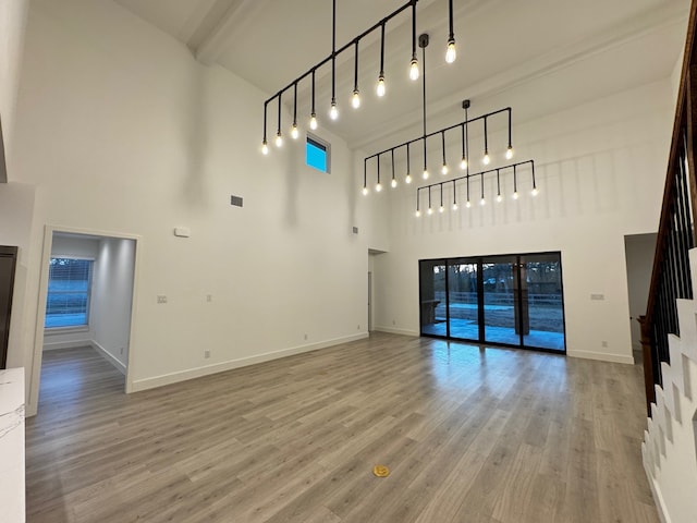 unfurnished living room featuring a high ceiling, wood-type flooring, track lighting, and beam ceiling