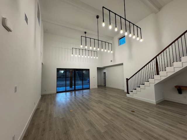 unfurnished living room with a towering ceiling, wood-type flooring, and beam ceiling