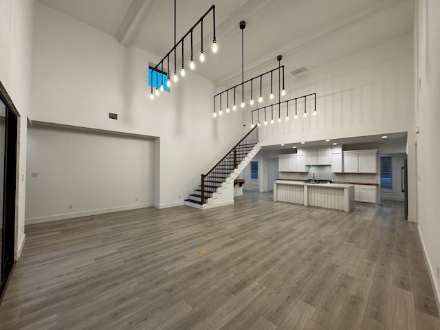 unfurnished living room featuring hardwood / wood-style flooring, beamed ceiling, and a high ceiling