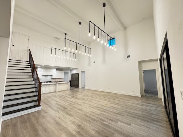 unfurnished living room with a towering ceiling, sink, beam ceiling, and light hardwood / wood-style flooring