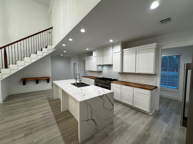 kitchen with sink, white cabinetry, light stone counters, double oven range, and a kitchen island with sink