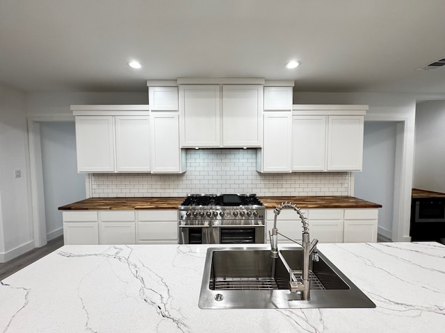 kitchen with white cabinetry, wood counters, decorative backsplash, and range with two ovens