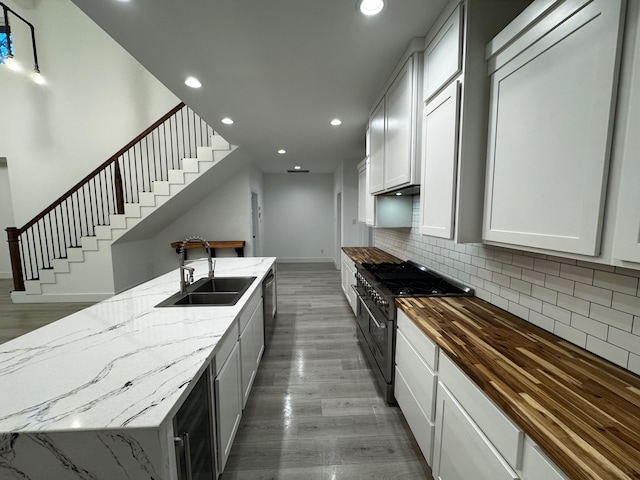 kitchen featuring high end stainless steel range, sink, light stone countertops, and white cabinets