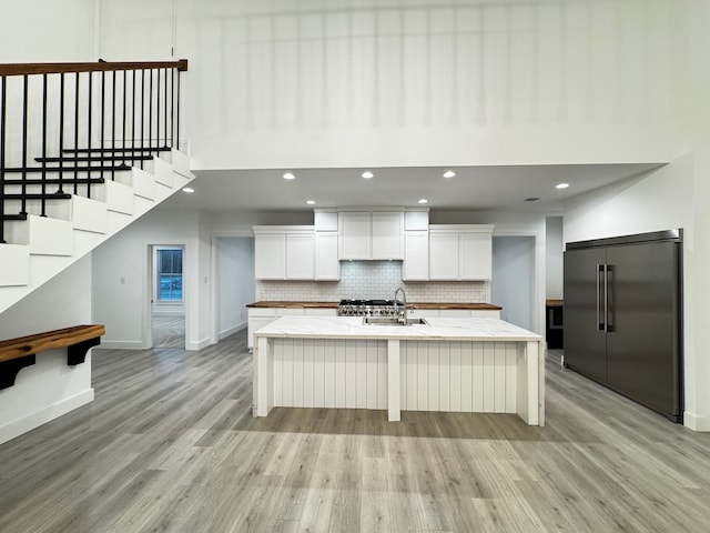 kitchen featuring built in fridge, white cabinets, decorative backsplash, a kitchen island with sink, and light hardwood / wood-style flooring