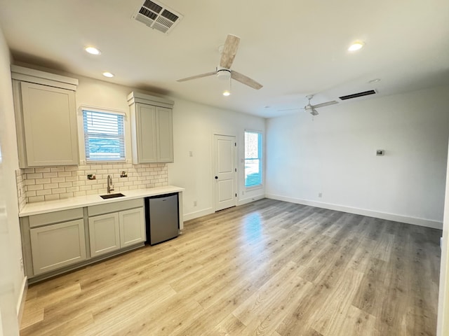 kitchen with dishwasher, sink, gray cabinetry, backsplash, and light wood-type flooring