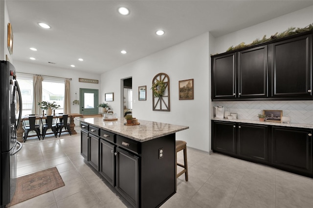 kitchen featuring a breakfast bar, black fridge, light stone counters, a center island, and backsplash