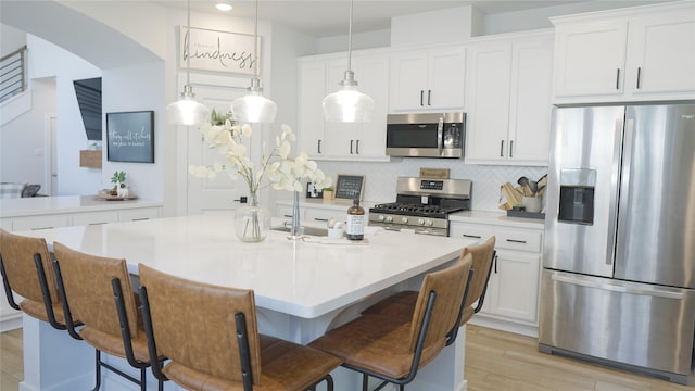 kitchen with a kitchen island with sink, stainless steel appliances, tasteful backsplash, white cabinets, and decorative light fixtures