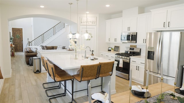 kitchen with sink, appliances with stainless steel finishes, hanging light fixtures, white cabinets, and a center island with sink