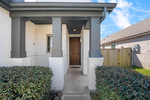 doorway to property with brick siding, covered porch, and fence