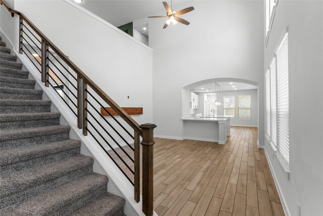 stairway with baseboards, a towering ceiling, wood finished floors, arched walkways, and a ceiling fan