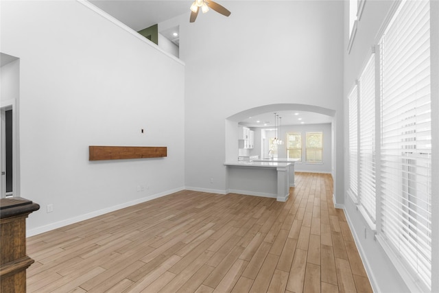 unfurnished living room featuring arched walkways, baseboards, a ceiling fan, and light wood-style floors