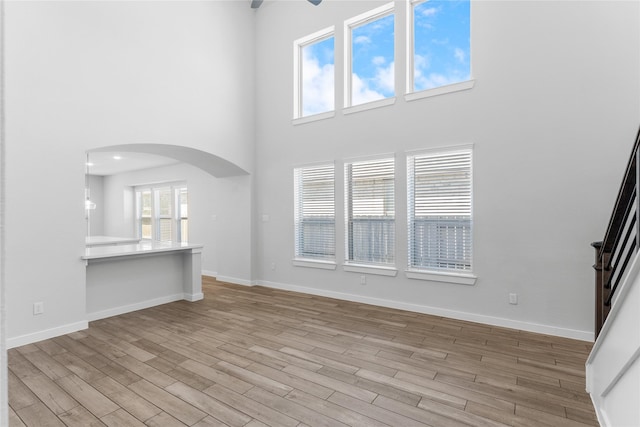 unfurnished living room with a ceiling fan, wood finished floors, baseboards, a high ceiling, and arched walkways