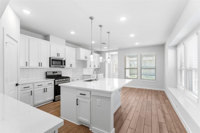 kitchen featuring tasteful backsplash, light countertops, light wood-type flooring, appliances with stainless steel finishes, and a sink