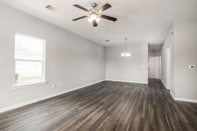 empty room with dark wood finished floors, visible vents, ceiling fan with notable chandelier, and baseboards