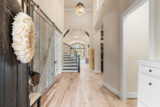 entrance foyer featuring arched walkways, stairway, a barn door, ornamental molding, and light wood-type flooring