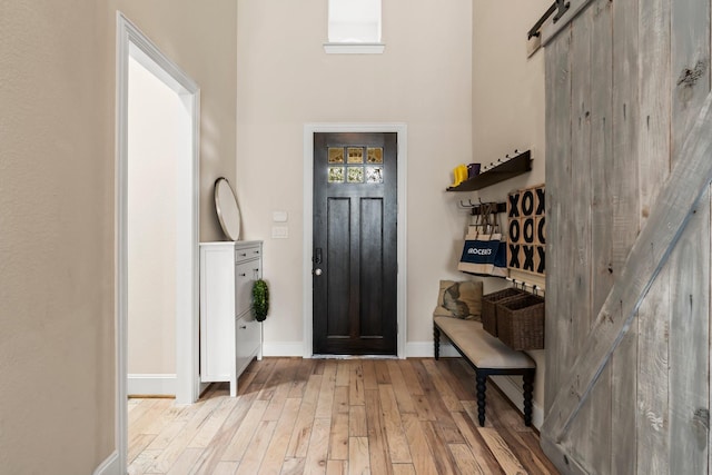 entryway featuring wood finished floors, a towering ceiling, baseboards, and a barn door