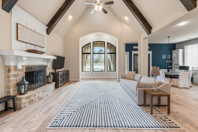 living area featuring ceiling fan, wood finished floors, beamed ceiling, a fireplace, and high vaulted ceiling