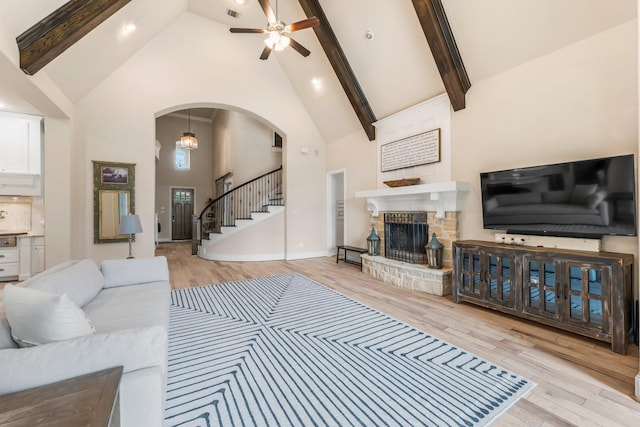 living room featuring arched walkways, a fireplace, wood finished floors, high vaulted ceiling, and stairs