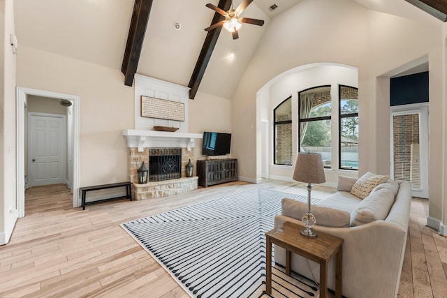 living area featuring high vaulted ceiling, a stone fireplace, wood finished floors, baseboards, and beam ceiling