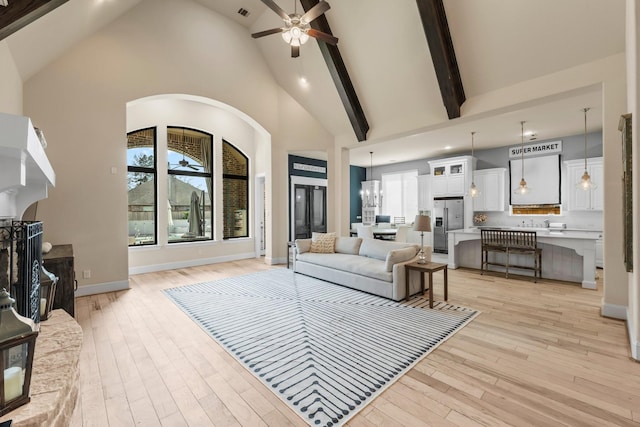 living area featuring ceiling fan with notable chandelier, high vaulted ceiling, light wood-type flooring, and a fireplace with raised hearth