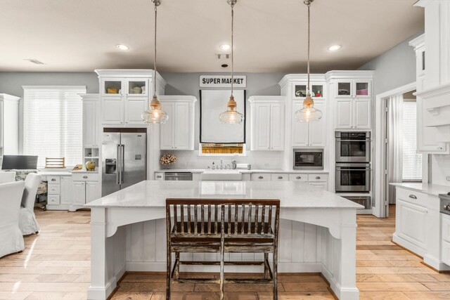 kitchen featuring white cabinets, a kitchen island, glass insert cabinets, appliances with stainless steel finishes, and a sink