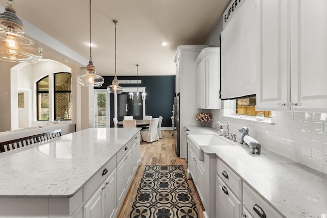 kitchen featuring decorative light fixtures, a center island, light stone countertops, white cabinetry, and backsplash