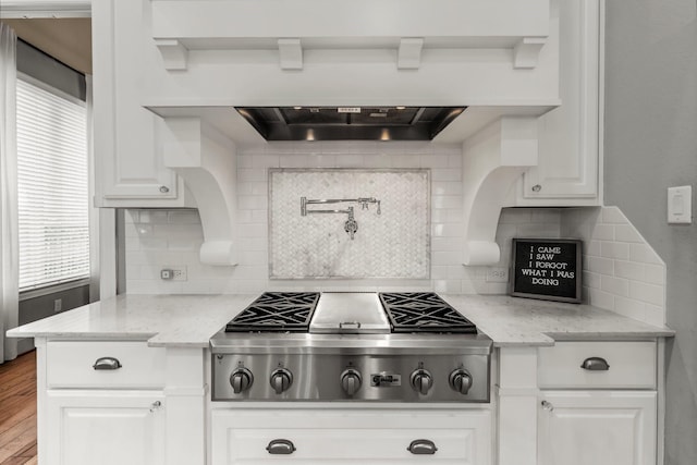 kitchen featuring light stone counters, decorative backsplash, white cabinets, and stainless steel gas stovetop