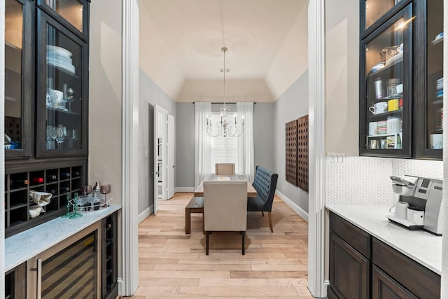 dining room featuring baseboards, a raised ceiling, light wood-style flooring, wine cooler, and an inviting chandelier