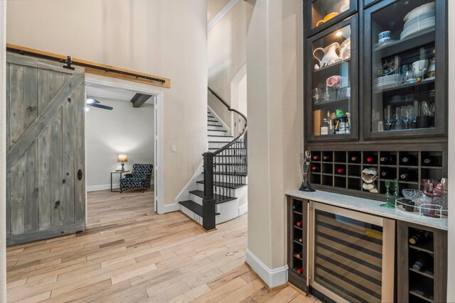 bar with wine cooler, light wood-style flooring, a barn door, baseboards, and stairs