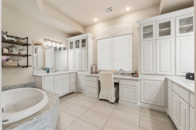 bathroom with visible vents, two vanities, a sink, and a jetted tub