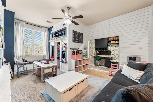 living room featuring wood walls, visible vents, a ceiling fan, and light colored carpet