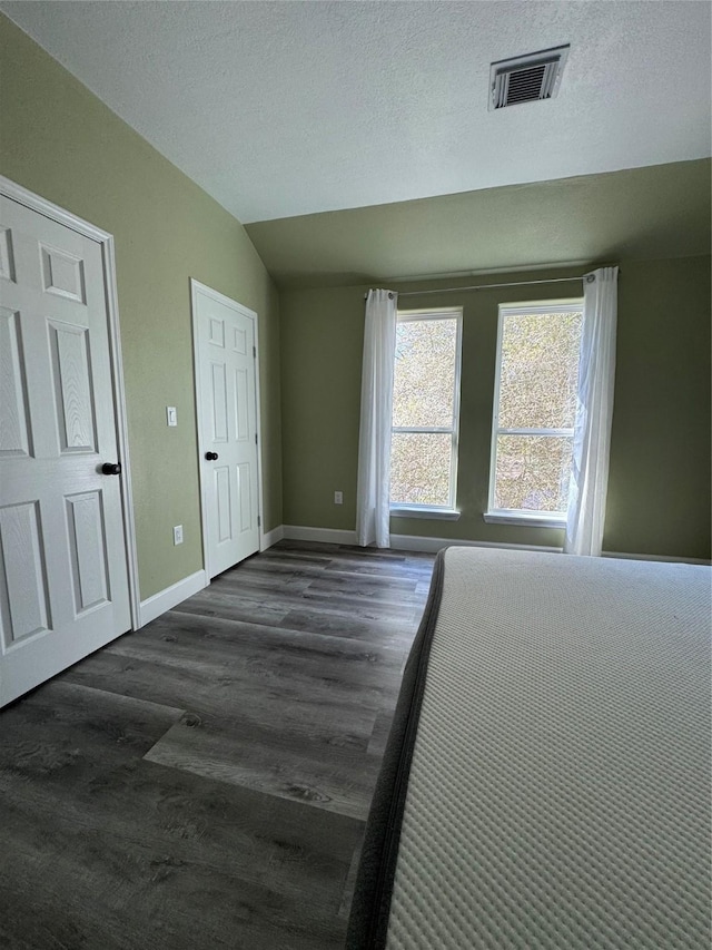 unfurnished bedroom featuring lofted ceiling, a textured ceiling, and dark hardwood / wood-style flooring