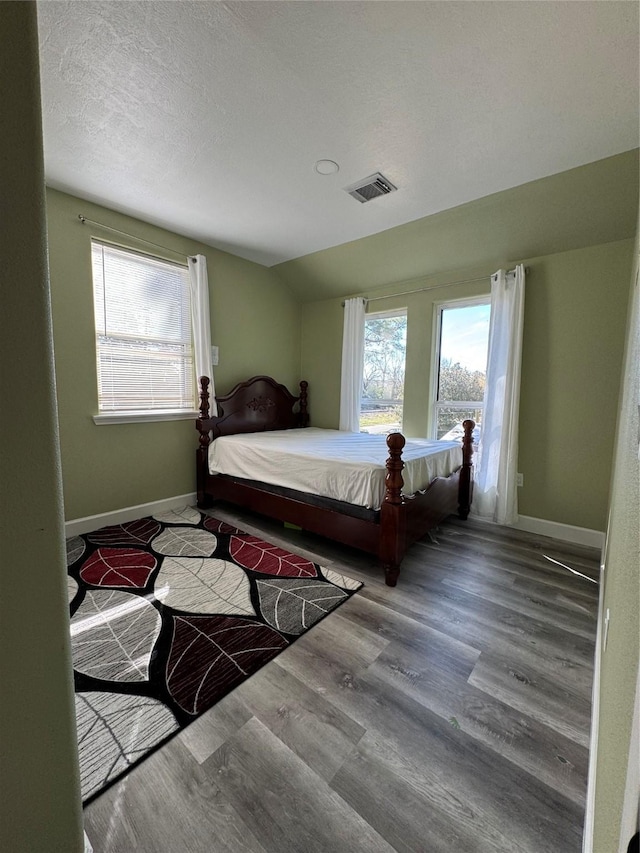 bedroom with lofted ceiling, multiple windows, wood finished floors, and visible vents