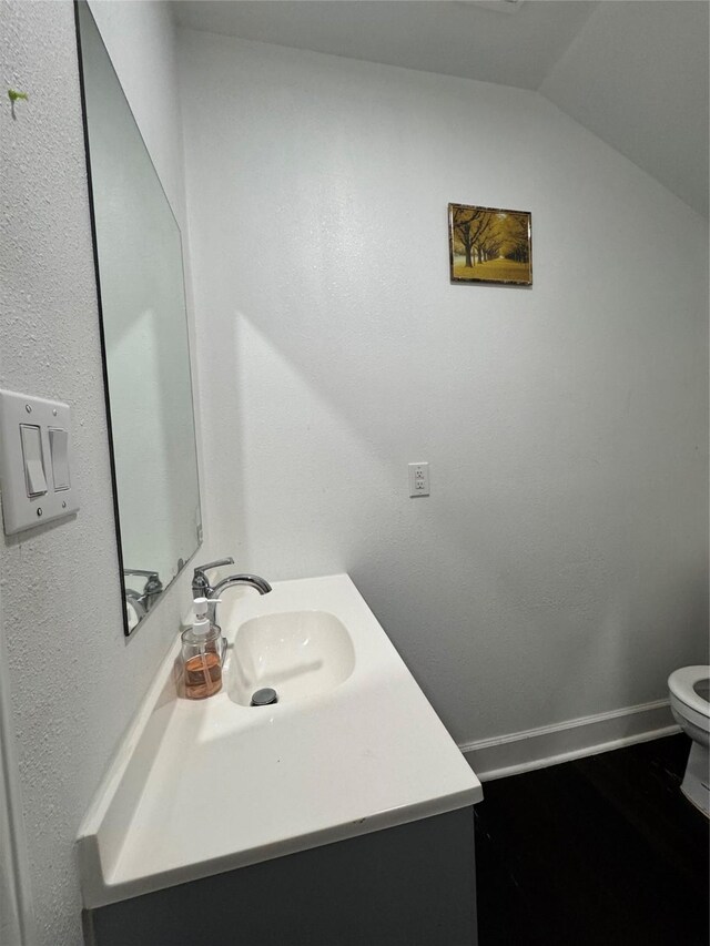 half bath featuring toilet, vanity, baseboards, and vaulted ceiling