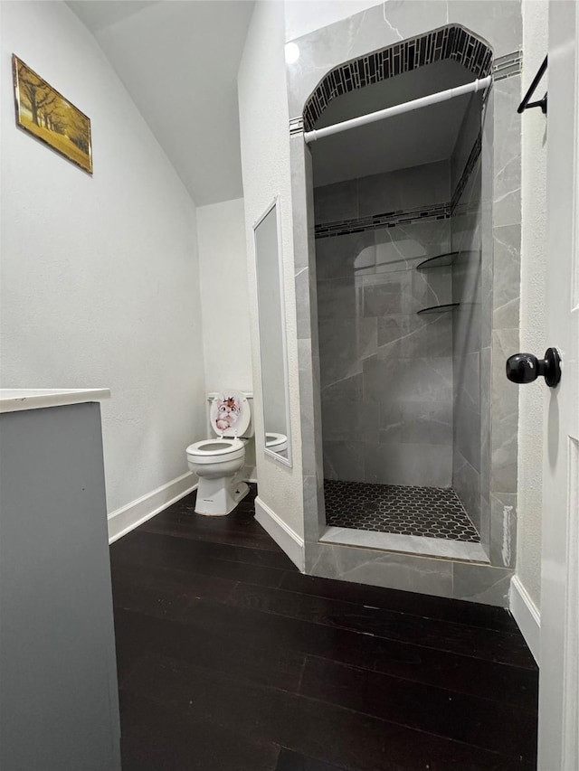 bathroom with baseboards, toilet, vaulted ceiling, a tile shower, and wood finished floors