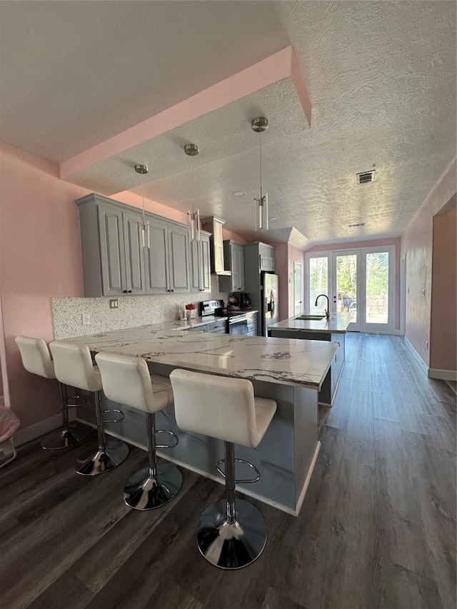 kitchen featuring a breakfast bar, appliances with stainless steel finishes, light stone countertops, decorative light fixtures, and wall chimney exhaust hood