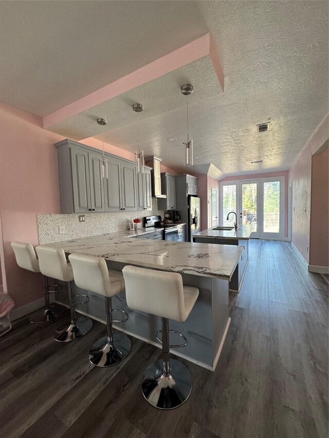 kitchen featuring a peninsula, gray cabinets, stainless steel range with electric stovetop, wall chimney range hood, and refrigerator with ice dispenser