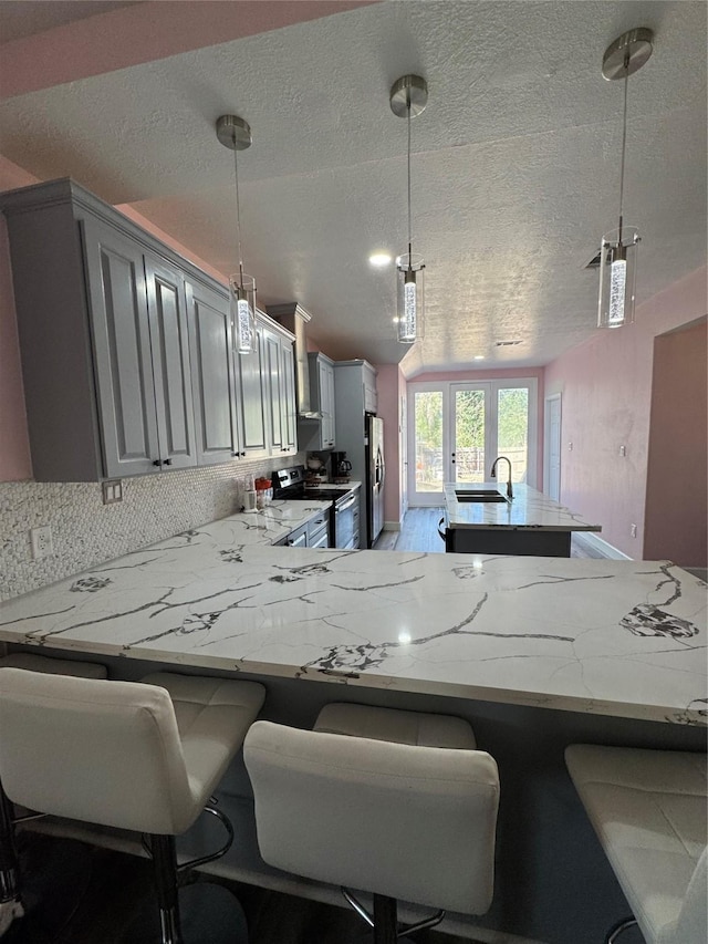 kitchen featuring gray cabinetry, stainless steel appliances, a peninsula, wall chimney range hood, and light stone countertops