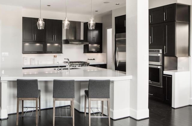 kitchen with wall chimney exhaust hood, decorative light fixtures, sink, and a breakfast bar area