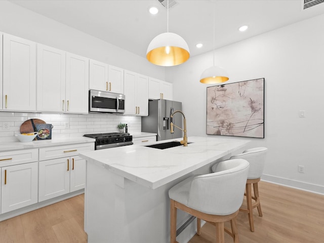 kitchen featuring pendant lighting, stainless steel appliances, a center island with sink, and white cabinets