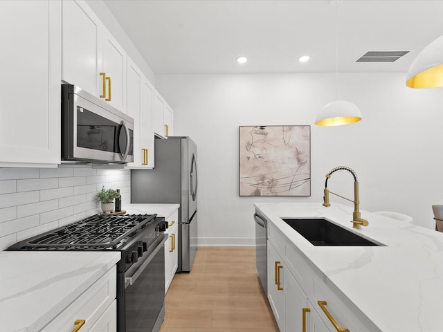 kitchen with white cabinetry, sink, hanging light fixtures, light stone counters, and stainless steel appliances