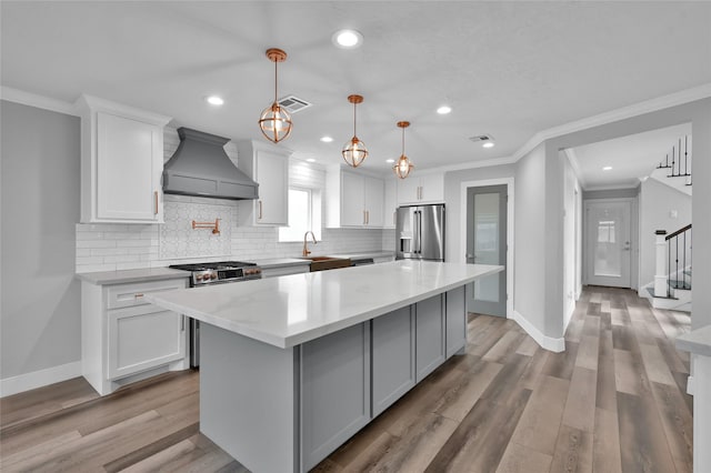 kitchen with custom exhaust hood, white cabinetry, high quality appliances, a kitchen island, and pendant lighting