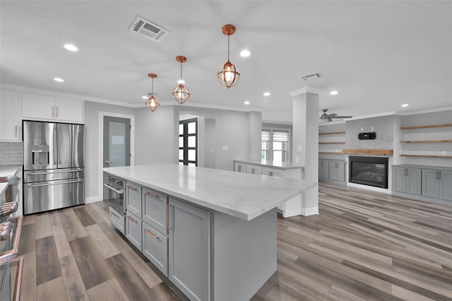 kitchen with pendant lighting, stainless steel appliances, a center island, light stone counters, and ornamental molding