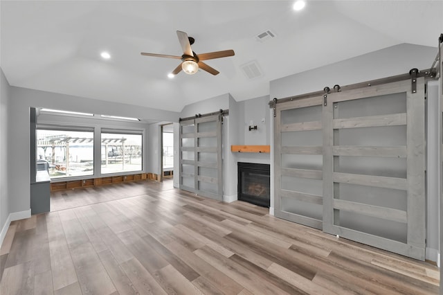 unfurnished living room with a barn door, lofted ceiling, ceiling fan, and light hardwood / wood-style flooring